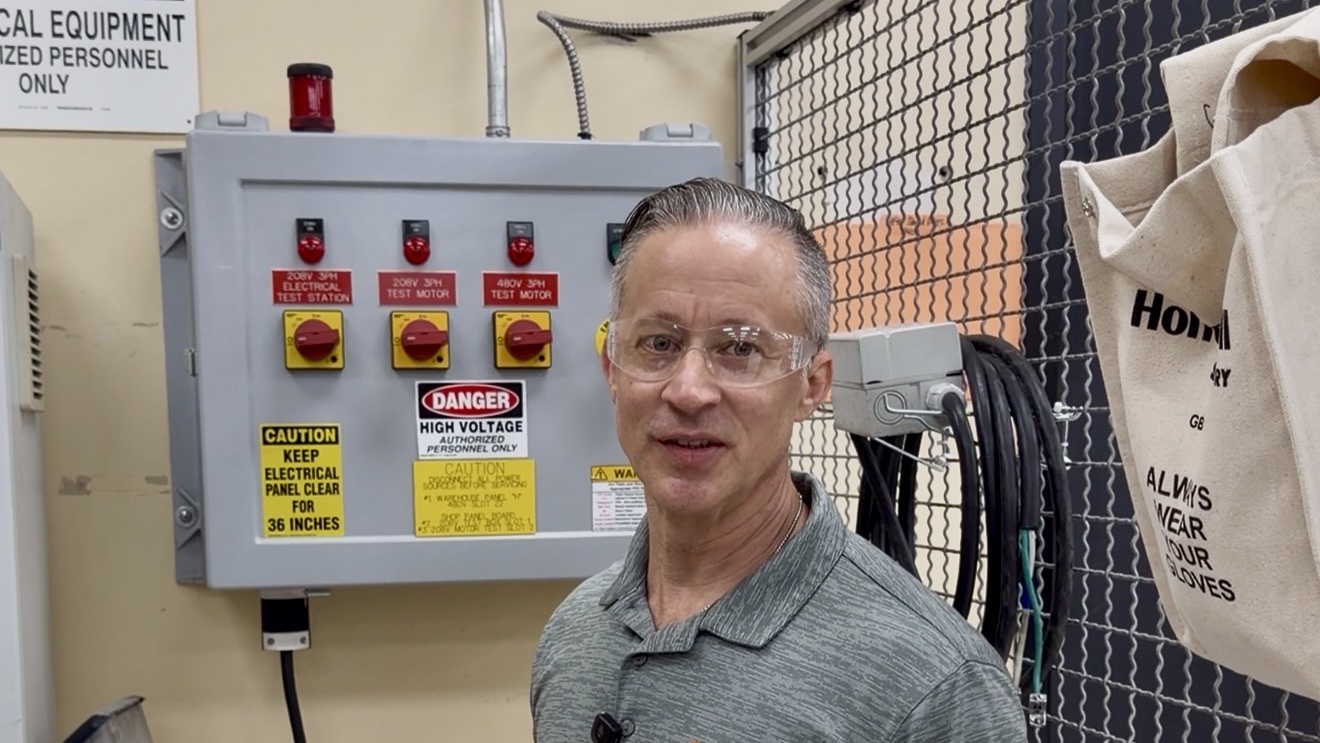 A Sprecher + Schuh team member standing beside a motor test panel in the applications lab